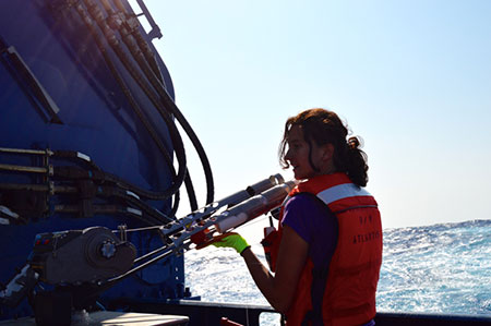 Alice Della Penna working with equipment on vessel with ocean in the background.